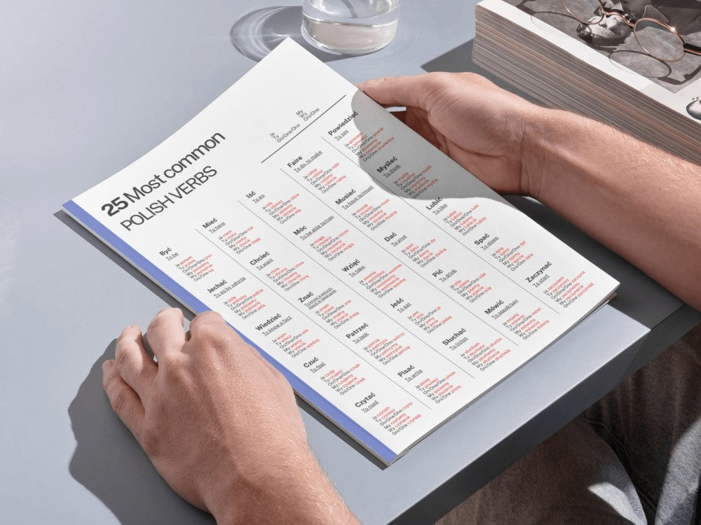 Person holding a book open to a page with text and tables on a light gray surface.