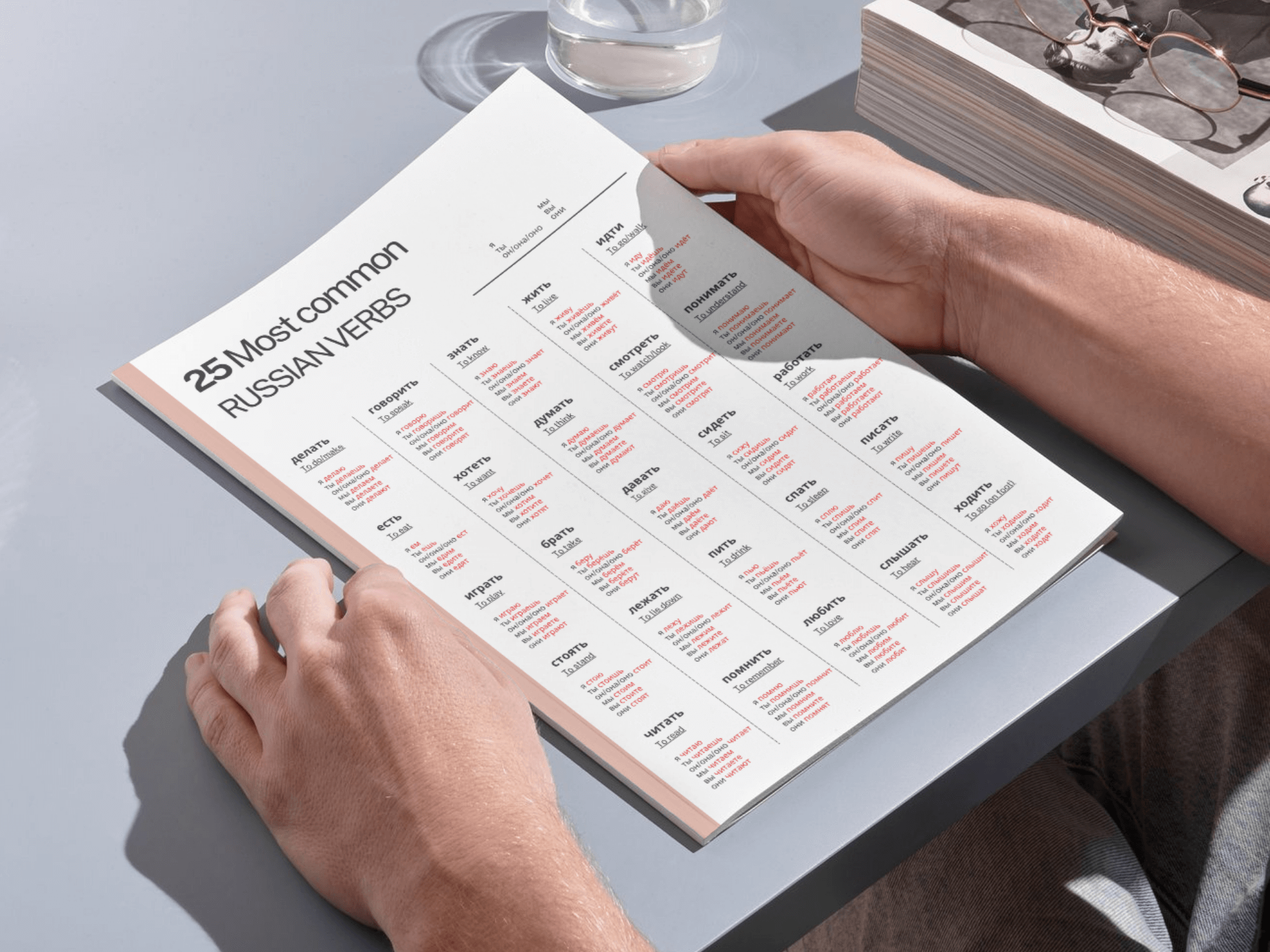 Person holding a book with Russian verb charts on a light gray surface