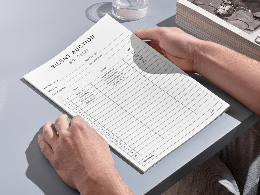 Person filling out a silent auction scorecard on a table.