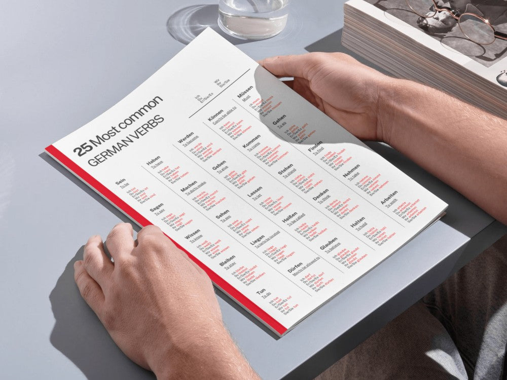 Person holding a book with German verb conjugations on a table.