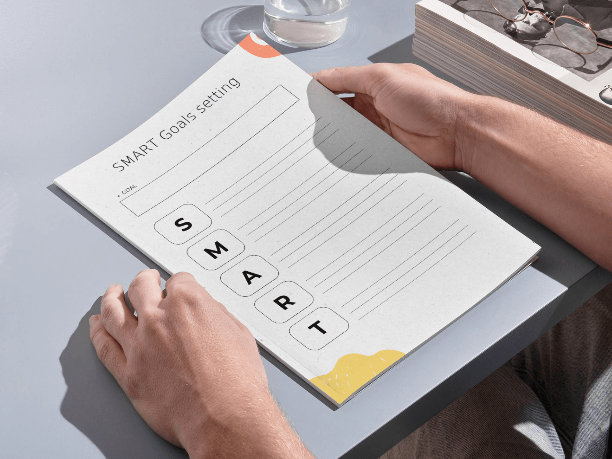 Person holding a notebook with 'SMART Goals setting' on a desk