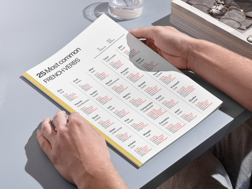Person holding a book with a French verb chart on a light gray surface