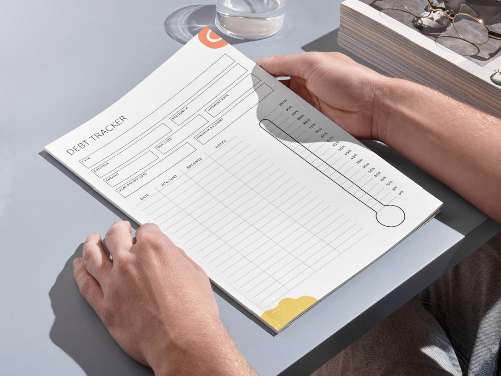 Person using a(debt tracker) on a desk with a glass of water and book in the background.