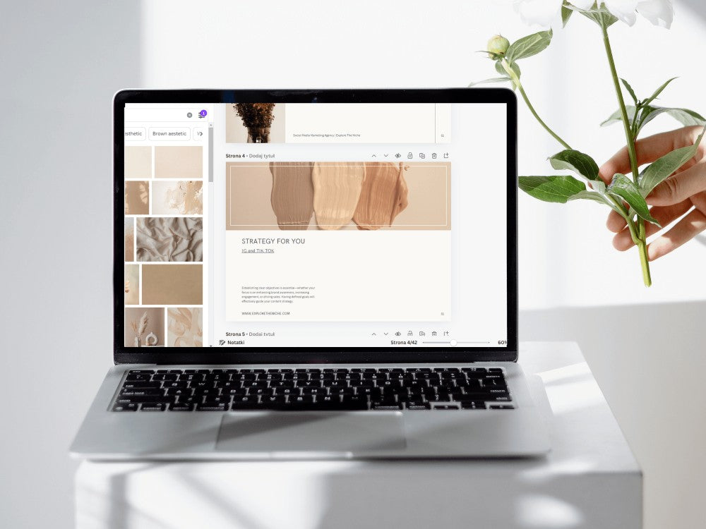 Laptop on a white surface with a website displayed, next to a hand holding a plant.