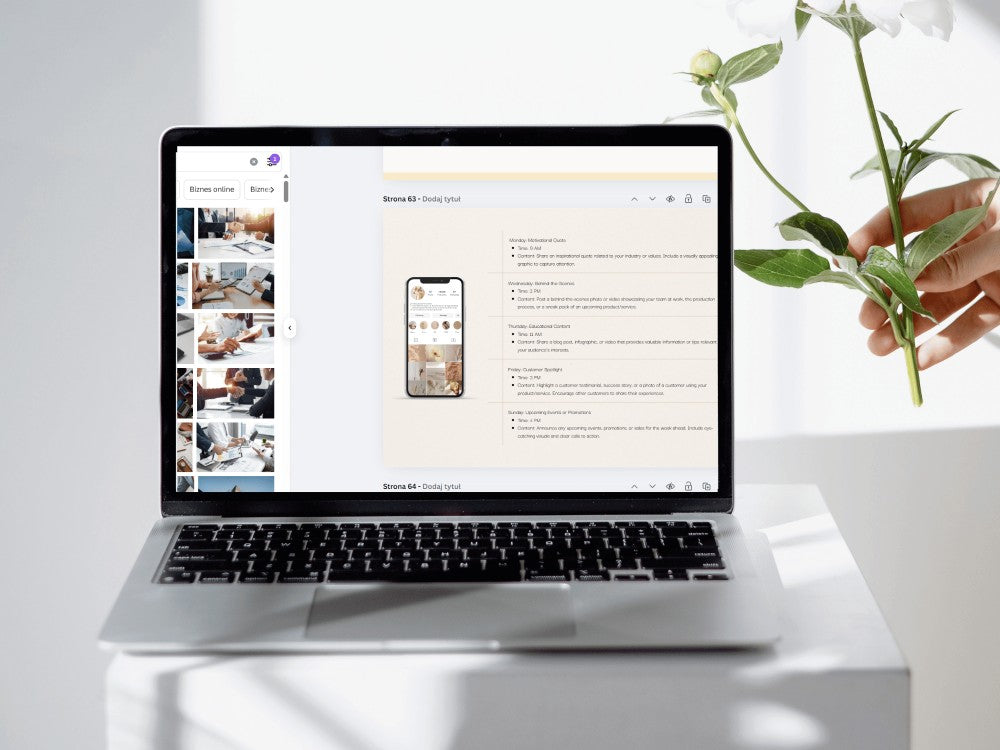 Laptop on a white surface with a hand holding a plant, displaying a website on the screen.