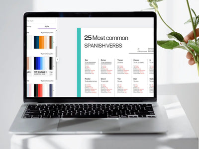 Laptop displaying a Spanish verb list on a white surface with a plant