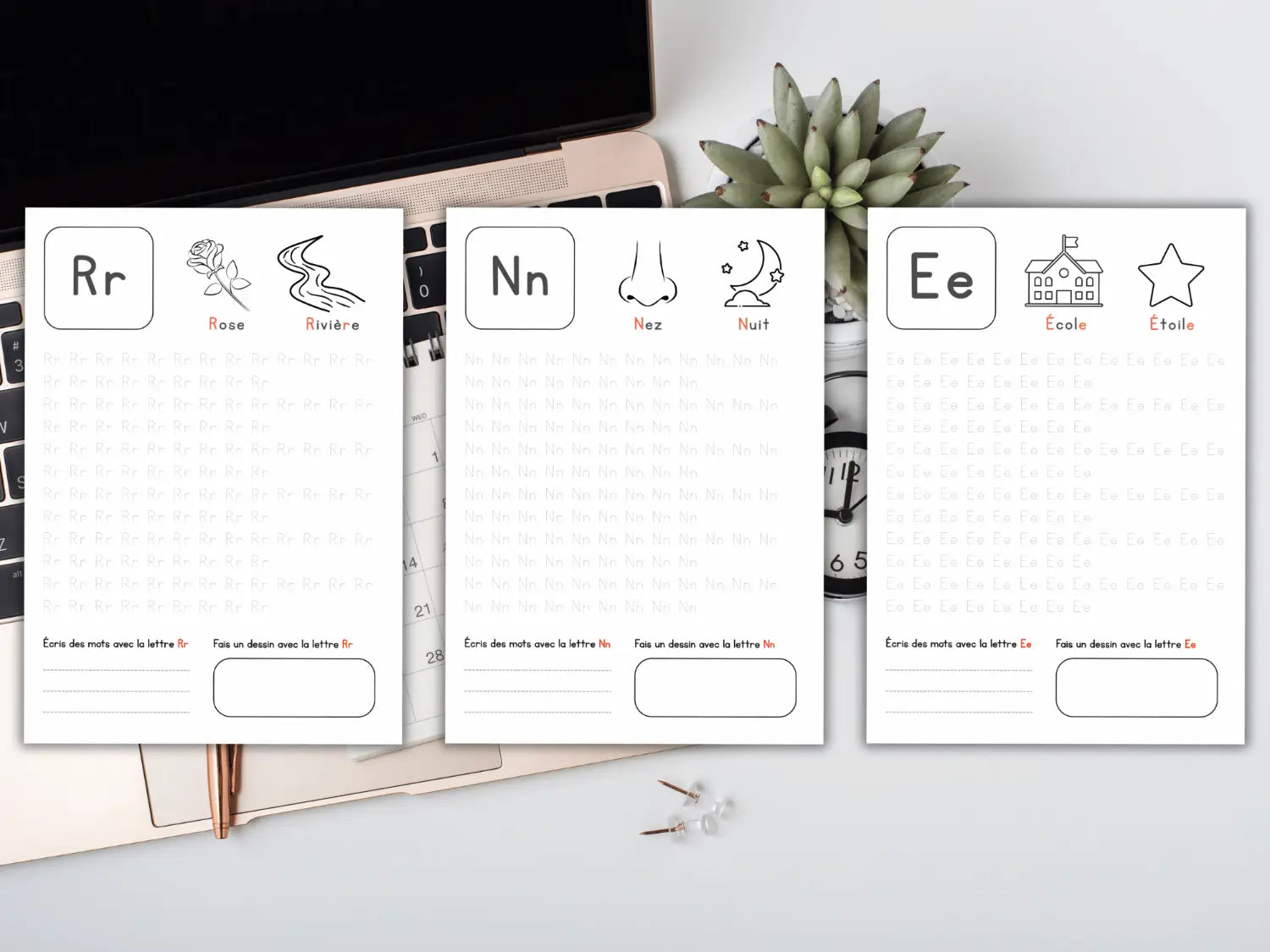 Three flashcards with letters R, N, and E on a desk with a computer and plant.