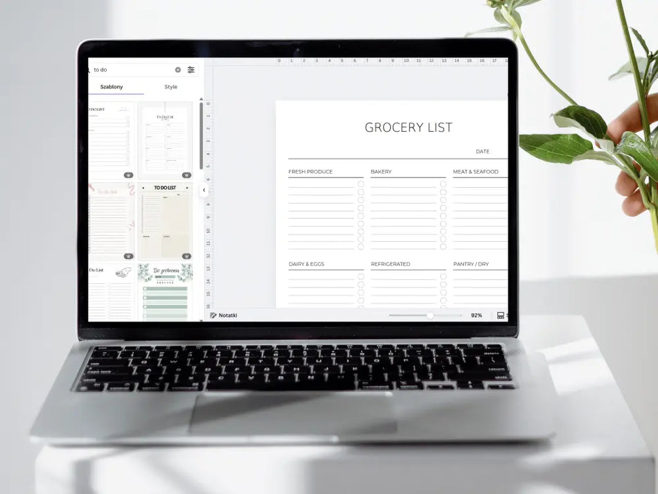 Laptop displaying a grocery list on a white surface with a plant