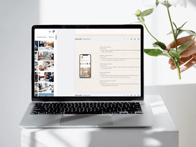 A silver laptop sits on a white pedestal, displaying a website mockup on its screen. A hand holding white flowers is visible on the right side of the frame against a bright, clean white background.