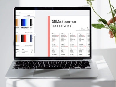 Laptop displaying a list of English verbs on a white surface with a plant.