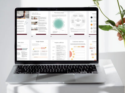 A silver laptop displays several pages of the business plan, including 