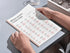 Person holding a book with Russian verb conjugation charts on a light gray surface.