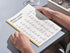 Person holding a book with a French vocabulary chart on a table.