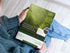A high-angle view of a person holding a physical, printed copy of the Landscaping Business Plan and Client Onboarding manual