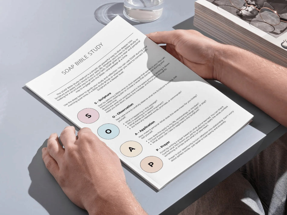 Person holding a book with a SOAP Bible Study format on a table.