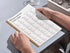 Person holding a book with Arabic vowels chart on a table