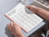 Person holding an open book with educational content on a table