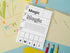 A printed worksheet titled 'Magic' with writing and coloring sections, laid on top of a pastel desk scene with colored pencils, paper envelopes, and a decorative card.