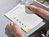 Person using a SMART goals tracker on a desk with a glass of water and book in the background.
