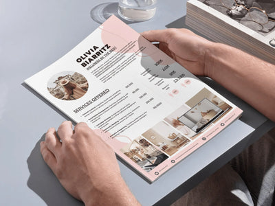 Person holding a pink and white business card with text and images on a gray surface