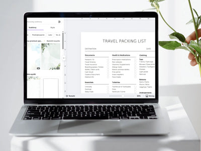 Laptop displaying a travel packing list on a white surface with a plant.