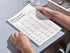 Person holding a tablet displaying a Portuguese verb chart on a light gray surface.