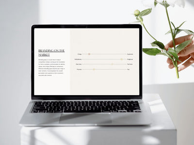 Laptop on a white surface with a hand holding a plant, displaying a branding document.