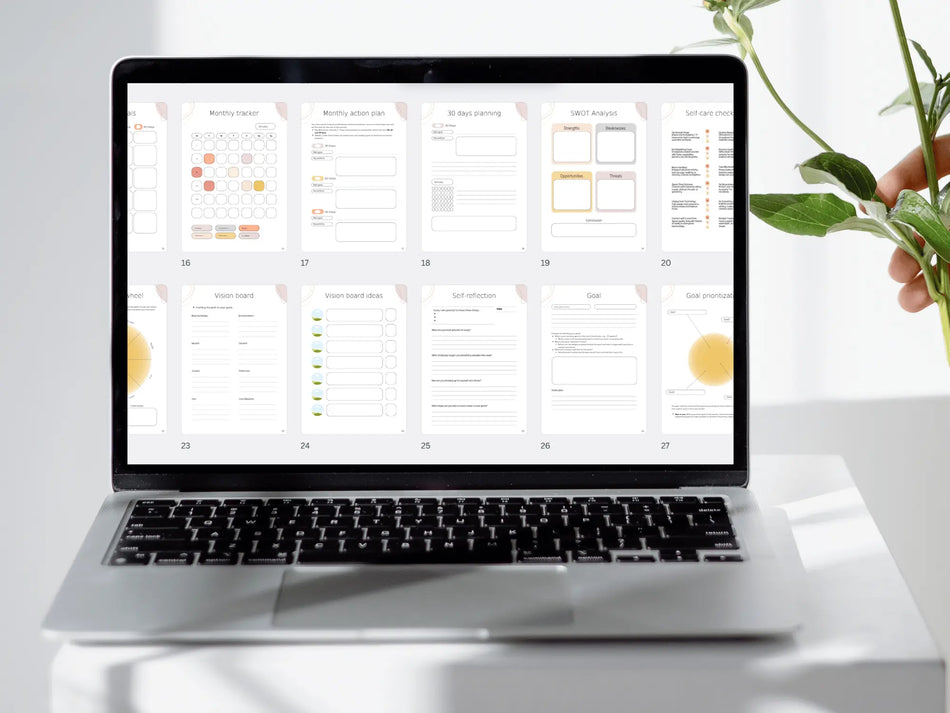 A close-up view of a laptop screen on a white desk showing a grid of 10 different planner pages including vision boards, self-reflection prompts, and goal prioritization charts