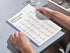 a person holding a printed version of the 25 most common polish verbs chart on a desk for physical study.