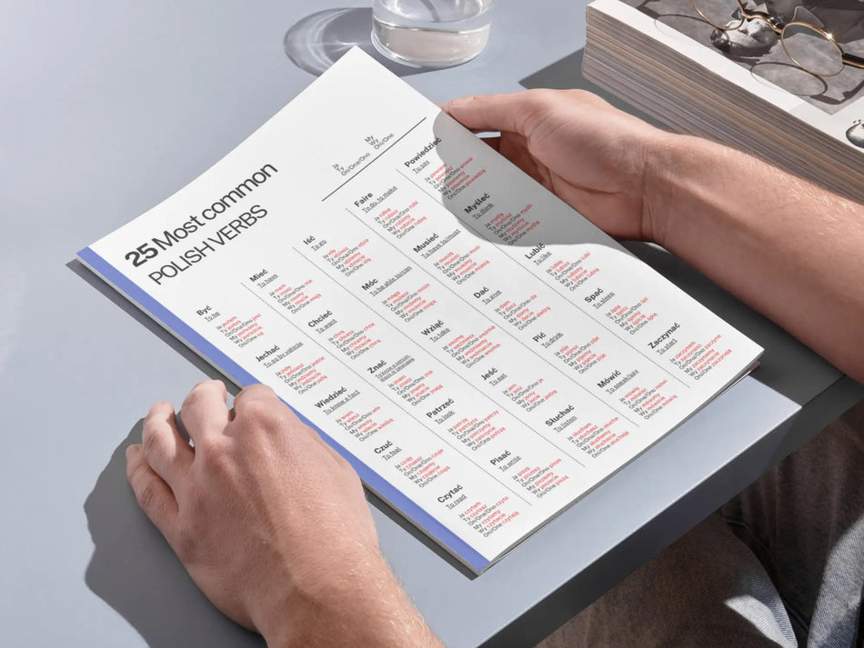 a person holding a printed version of the 25 most common polish verbs chart on a desk for physical study.